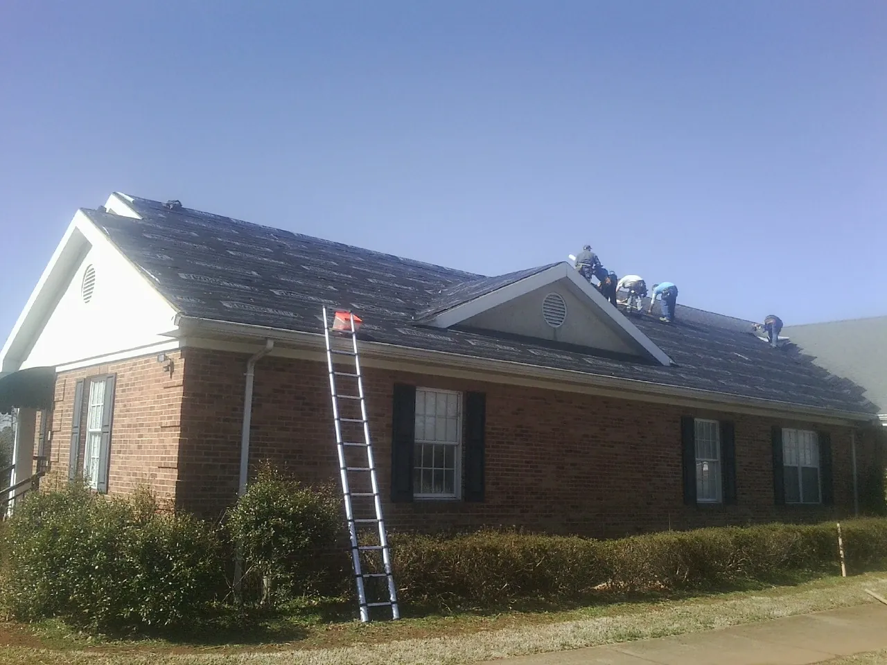 Crew tearing shingles off a brick ranch roof with a ladder set — Emergency Roof Repair work by our crew in Chagrin Falls