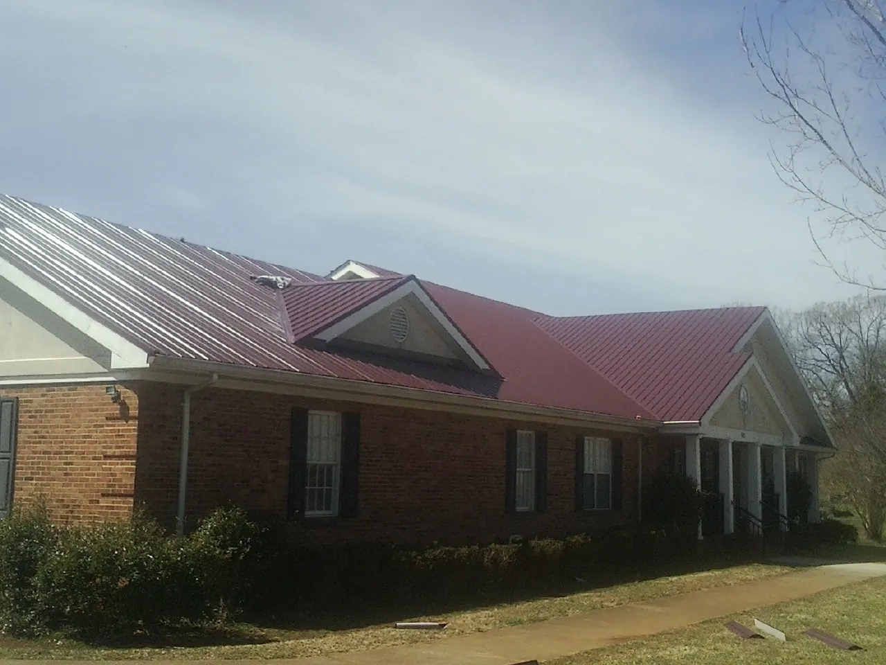 Red metal roof with gabled entries on a long brick building, from a Hail Damage Roof Repair job in Chagrin Falls