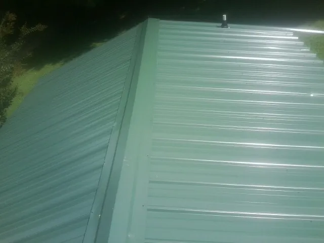 New green metal panels meeting at the ridge of a roof — Flat Roof Repair work by our crew in Chagrin Falls