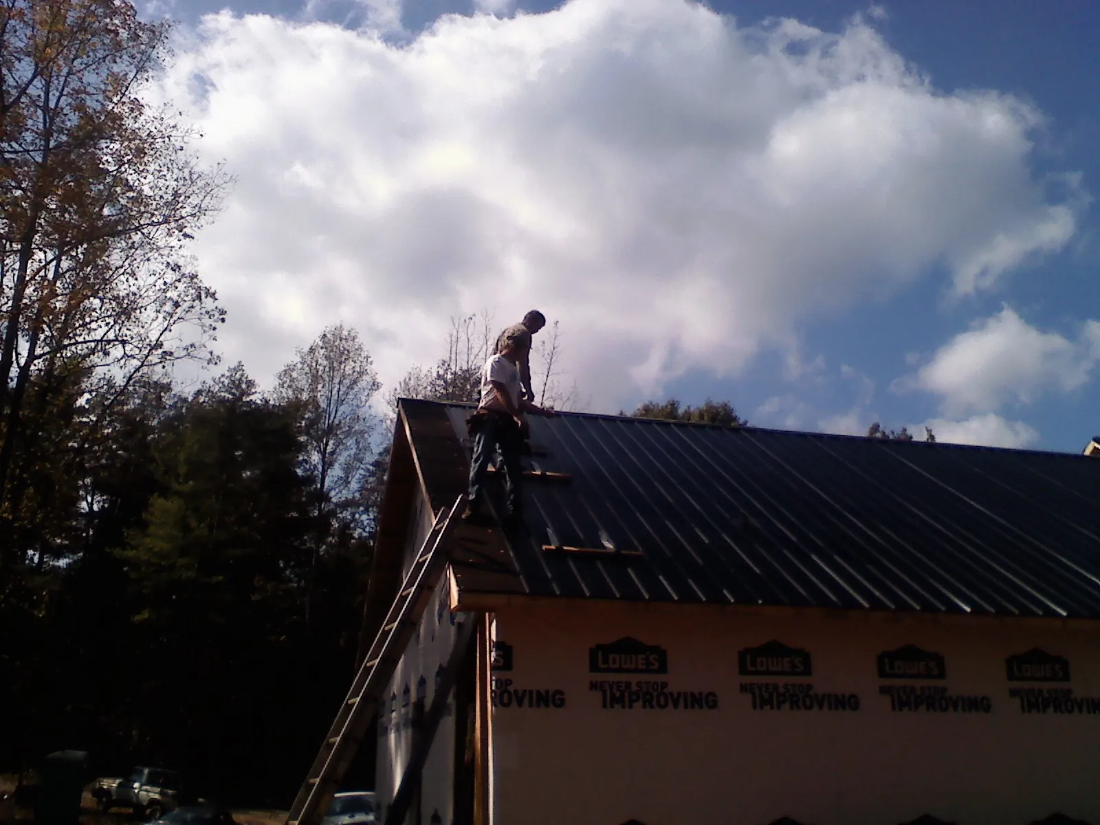 Roofer fastening dark metal panels high against a cloudy sky, from a Roof Inspection job in Chagrin Falls