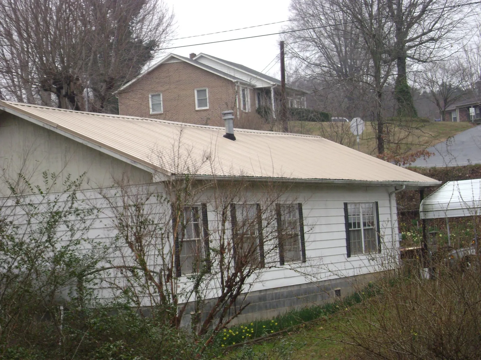 Tan metal roof on a white sided house set into a hillside — Commercial Roofing by Roofing Brothers in Chagrin Falls